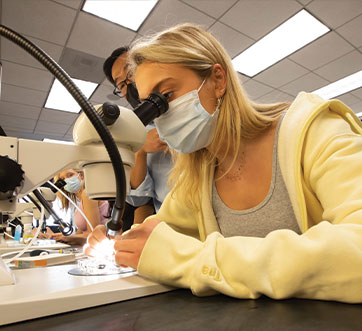 Photo of student looking through a microscope. Links to Gifts That Pay You Income